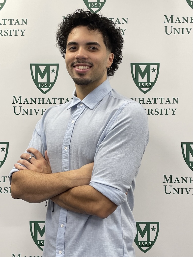 David Pozo, a Manhattan University student, standing with arms crossed in front of a Manhattan University backdrop.